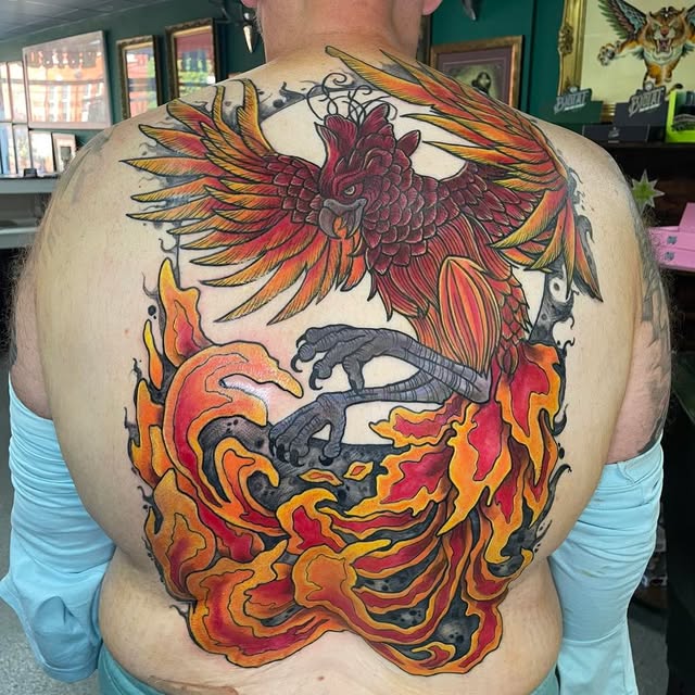 Large red and gold bird tattoo across a back, with grey claws and sweeping orange flames