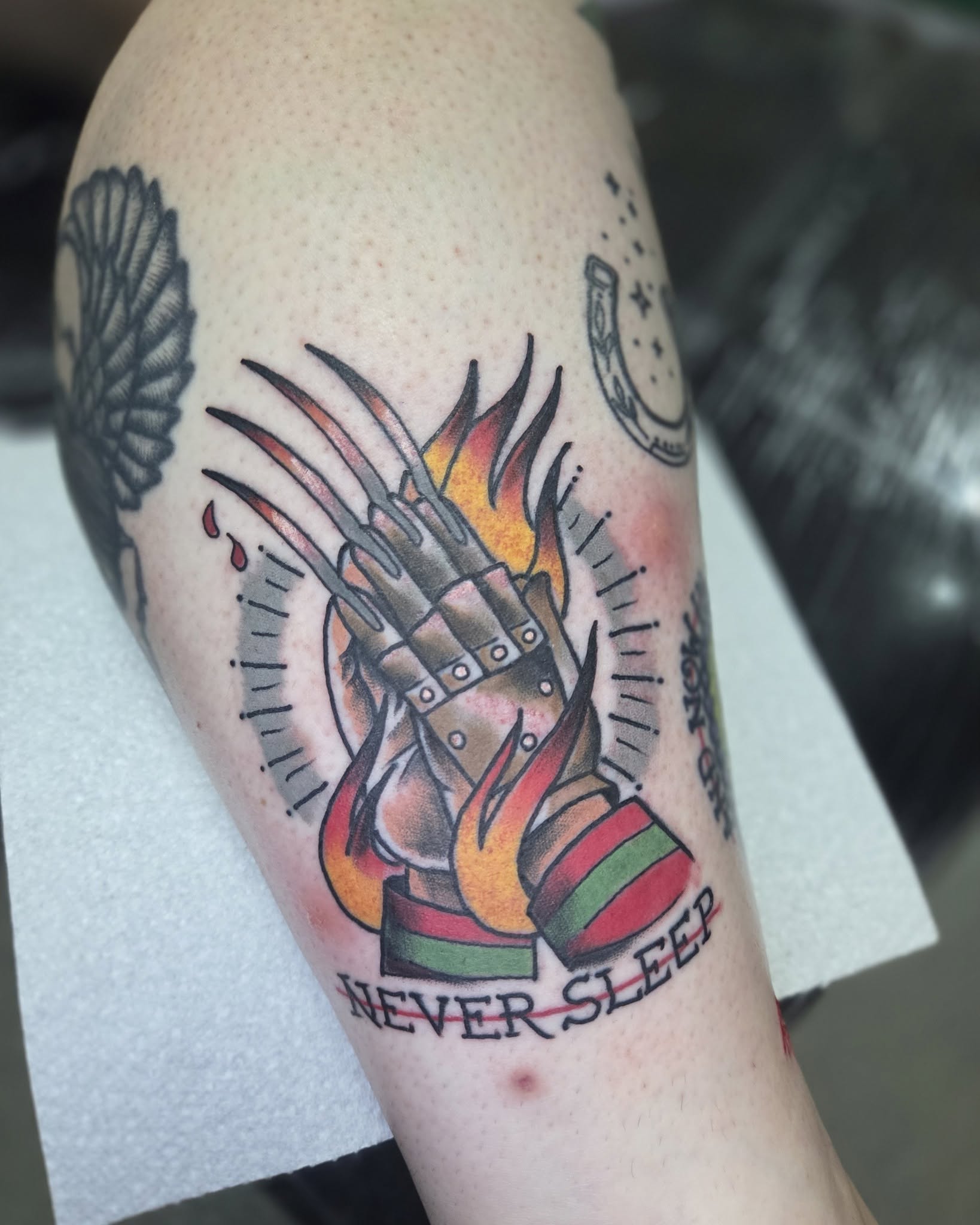 A bladed glove tattoo surrounded by orange flames, by Dan